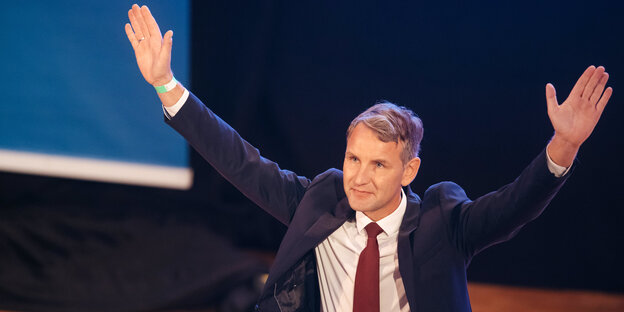 Björn Höcke streckt auf einer Bühne die Arme aus