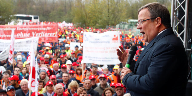 Armin Laschet steht auf einer Bühne vor den DemonstrantInnen