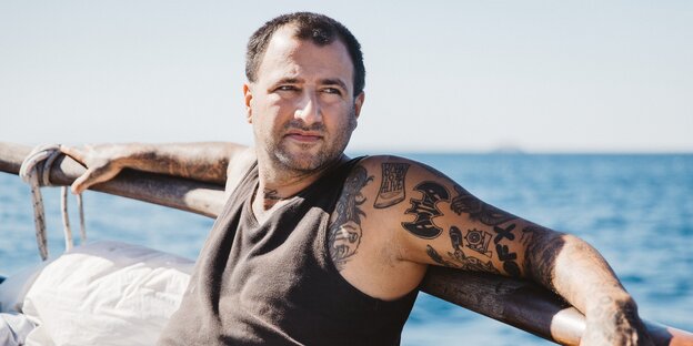Kapitän Dariush angelehnt an eine Schiffsreling, hinter ihm das Meer Kapitän Dariush angelehnt an eine Schiffsreling, hinter ihm das Meer