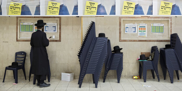 Ein ultraorthodoxer Jude steht in einem Gebäude an einer Wand mit Wahlplakaten Ein ultraorthodoxer Jude steht in einem Gebäude an einer Wand mit Wahlplakaten