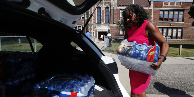 Eine Frau trägt in Plastik eingeschweißte Wasserflaschen in einen Kofferraum Eine Frau trägt in Plastik eingeschweißte Wasserflaschen in einen Kofferraum