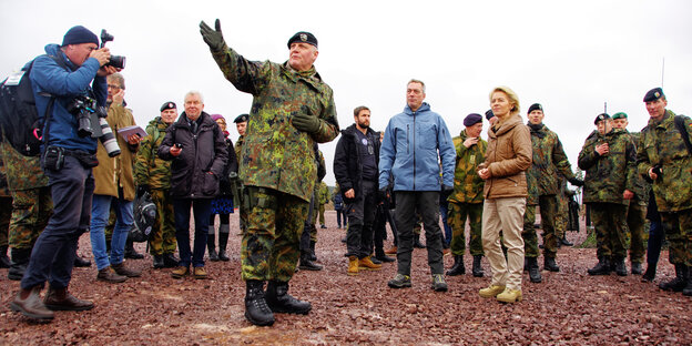 Mehrere Menschen, einige davon in Uniform, stehen auf steinigem Boden Mehrere Menschen, einige davon in Uniform, stehen auf steinigem Boden