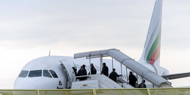 Ein Flugzeug mit einer Treppe davor. Darauf stehen Polizisten