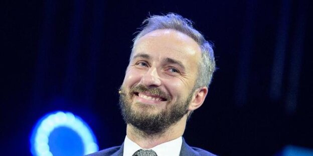 Moderator Jan Böhmermann in blauem Anzug grinsend vor dunklem Hintergrund