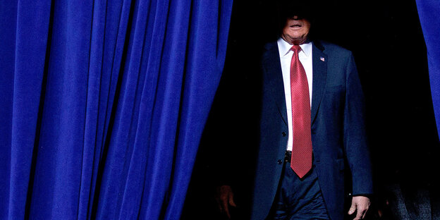 Trump tritt hinter einem blauen Vorhang hervor, das Scheinwerferlicht beleuchtet von seinem Gesicht nur den Mund Trump tritt hinter einem blauen Vorhang hervor, das Scheinwerferlicht beleuchtet von seinem Gesicht nur den Mund