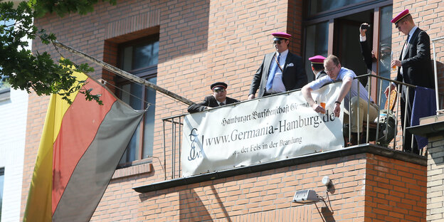Herren in komischer Kleidung stehen auf einem Balkon und präsentieren die aktuelle Deutschland-Fahne Herren in komischer Kleidung stehen auf einem Balkon und präsentieren die aktuelle Deutschland-Fahne
