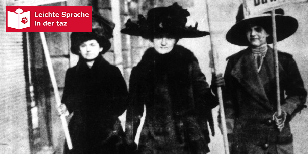 Ein Schwarz-Weiß-Bild zeigt drei Frauen, die mit Schildern auf der Straße laufen und für den Wahlgang Werbung machen Ein Schwarz-Weiß-Bild zeigt drei Frauen, die mit Schildern auf der Straße laufen und für den Wahlgang Werbung machen