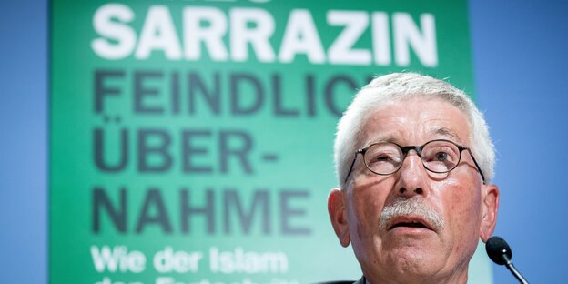 Thilo Sarrazin im Vordergrund, eine grüne Wand mit schwarzer und weißer Schrift im Hintergrund