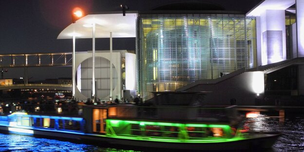 Ein beleuchtets Bundestagsgebäude bei Nacht und ein bunt beleuchtets kleines Schiff davor Ein beleuchtets Bundestagsgebäude bei Nacht und ein bunt beleuchtets kleines Schiff davor