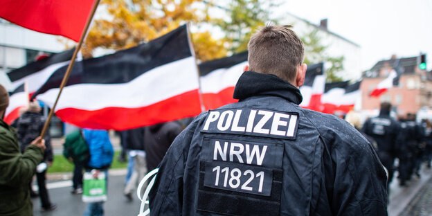 Ein Polizist vor einem Demonstrationszug mit schwarz.weiß-roten Fahnen Ein Polizist vor einem Demonstrationszug mit schwarz.weiß-roten Fahnen