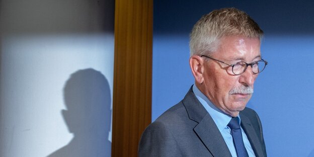 Thilo Sarrazin trägt einen Anzug und läuft nach rechts, im Hintergrund ist sein Schatten zu sehen