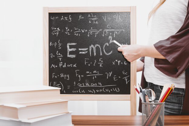 Eine Person mit einem Kreidestück in der Hand steht neben einer Tafel, die mit Formeln beschrieben ist Eine Person mit einem Kreidestück in der Hand steht neben einer Tafel, die mit Formeln beschrieben ist