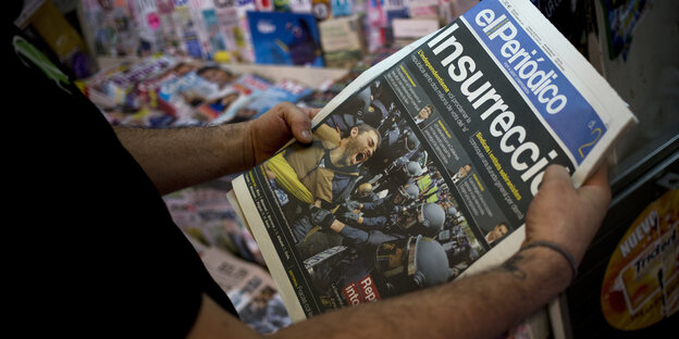 Zwei Hände halten eine Zeitung. Darauf ist ein Foto Auseinandersetzungen mit der Polizei zu sehen Zwei Hände halten eine Zeitung. Darauf ist ein Foto Auseinandersetzungen mit der Polizei zu sehen