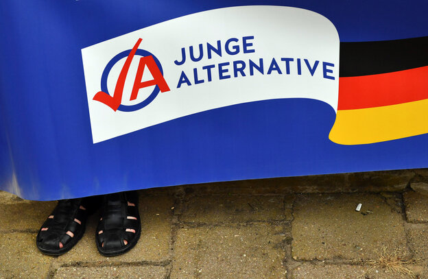 Schwarze Herrensandalen schauen unter einem Plakat der Jungen Alternativen hervor Schwarze Herrensandalen schauen unter einem Plakat der Jungen Alternativen hervor