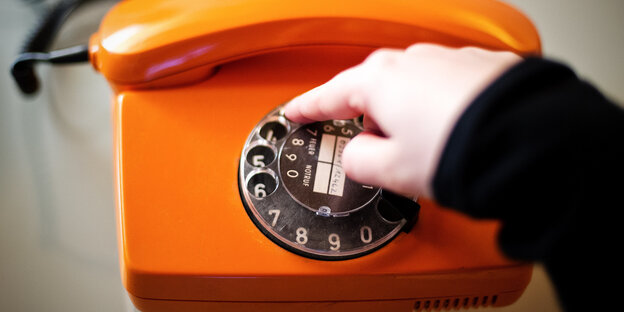 Ein Finger bedient ein oranges Wählscheibentelefon Ein Finger bedient ein oranges Wählscheibentelefon