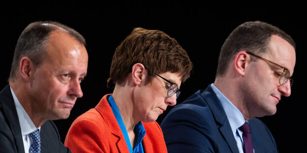 Friedrich Merz, Annegret Kramp-Karrenbauer und Jens Spahn sitzen auf der Bühne die Köpfe nach unten geneigt. Friedrich Merz, Annegret Kramp-Karrenbauer und Jens Spahn sitzen auf der Bühne die Köpfe nach unten geneigt.