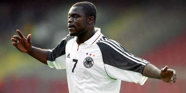 Gerald Asamoah, ein Mann mit dunkler Hautfarbe hat ein Deutschland-Trikot an und breitet beide Arme aus Gerald Asamoah, ein Mann mit dunkler Hautfarbe hat ein Deutschland-Trikot an und breitet beide Arme aus