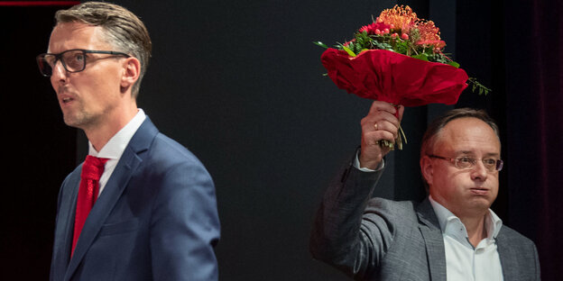 Zwei Männer, einer hebt einen Blumenstrauß hoch Zwei Männer, einer hebt einen Blumenstrauß hoch