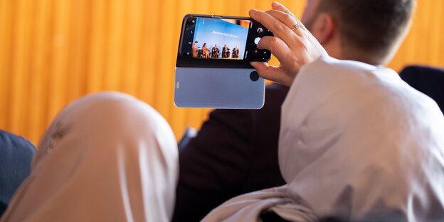 Von hinten sind zwei Frauen mit Kopftuch zu sehen, die mit ihrem Handy eine Podiumsdiskussion auf der Islamkonferenz fotografieren Von hinten sind zwei Frauen mit Kopftuch zu sehen, die mit ihrem Handy eine Podiumsdiskussion auf der Islamkonferenz fotografieren
