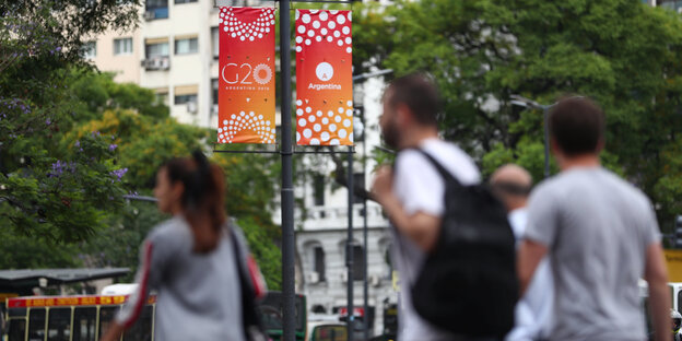 Menschen laufen in einer Stadt vor einem G20-Banner lang Menschen laufen in einer Stadt vor einem G20-Banner lang