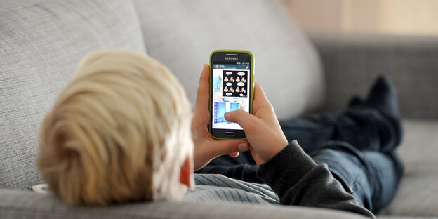 Jemand liegt auf einem Sofa und schaut auf ein Smartphone Jemand liegt auf einem Sofa und schaut auf ein Smartphone