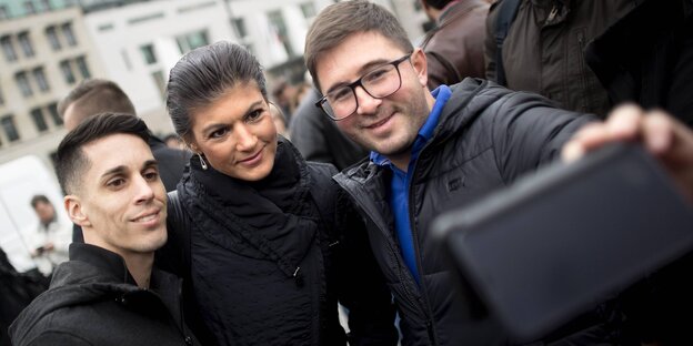 Sahra Wagenknecht zwischen zwei Männern, die mit ihr ein Selfie schießen, bei einer Demo von „Aufstehen“