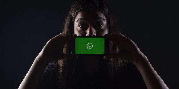 Frau hält Smartphone mit Whatsapp-Symbol vor ihren Mund Frau hält Smartphone mit Whatsapp-Symbol vor ihren Mund