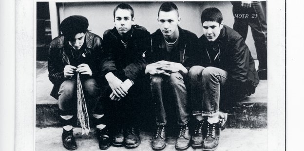 Ein schwarz-weiß Foto, auf dem vier junge Männer, die Band "Beastie Boys" nebeneinander sitzen