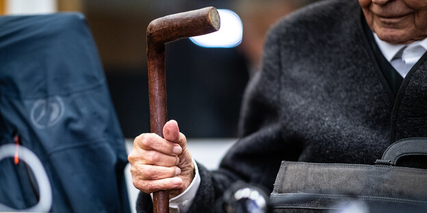 Sitzender alter Mann hält sich an Gehstock fest