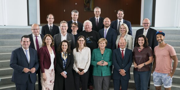 Menschen stehen nebeneinander und posieren für ein Foto, darunter Angela Merkel und Ijad Madisch, der ein Superman-Cap und kurze Hosen trägt Menschen stehen nebeneinander und posieren für ein Foto, darunter Angela Merkel und Ijad Madisch, der ein Superman-Cap und kurze Hosen trägt