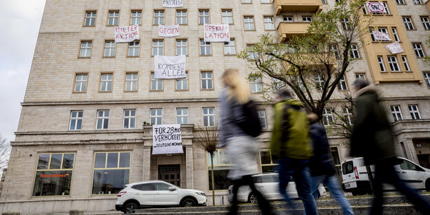 Menschen gehen vor einem Hochhaus in der Karl-Marx-Allee in Berlin