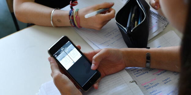 Schüler sitzt mit Handy am Tisch, daneben Schulunterlagen Schüler sitzt mit Handy am Tisch, daneben Schulunterlagen