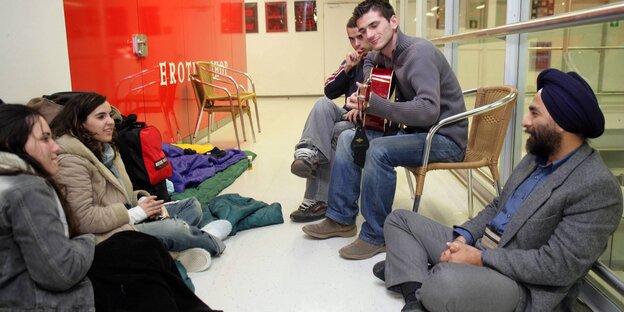 Verschiedene Menschen sitzen zusammen, einer spielt Gitarre Verschiedene Menschen sitzen zusammen, einer spielt Gitarre