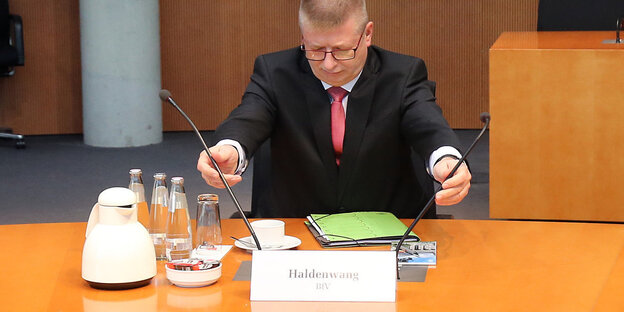 Verfassungsschutzchef Thomas Haldenwang sitzt an einem Tisch und richtet zwei Mikrofone Verfassungsschutzchef Thomas Haldenwang sitzt an einem Tisch und richtet zwei Mikrofone