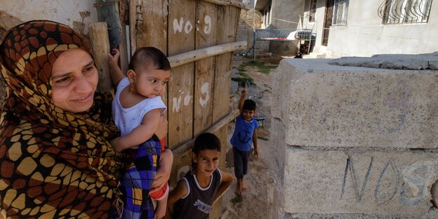 Eine Frau mit drei Kindern vor einem schlichten Haus