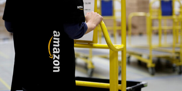 Eine Angestellte im Lager von Amazon schiebt einen Wagen