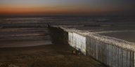 Menschen stehen an der Grenzmauer zwischen Mexiko und San Diego, Kalifornien, als die Sonne in Playas de Tijuana über dem Strand untergeht