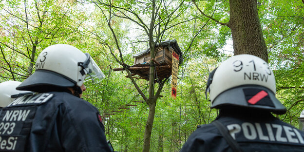 Zwei behelmte Polizisten stehen vor einem Baumhaus in einem Wald Zwei behelmte Polizisten stehen vor einem Baumhaus in einem Wald