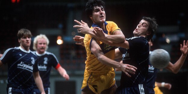 En Handballspieler im gelben Trikot wird umringt und angegangen von Spielern im dunklen Trikot En Handballspieler im gelben Trikot wird umringt und angegangen von Spielern im dunklen Trikot