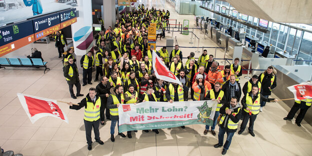 Mitglieder der Gewerkschaft Verdi stehen mit Fahnen am Flughafen in einem Terminal Mitglieder der Gewerkschaft Verdi stehen mit Fahnen am Flughafen in einem Terminal