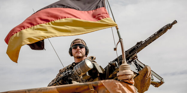 Ein Soldat auf einem Stützpunkt mit Deutschlandflagge und Maschinengewehr Ein Soldat auf einem Stützpunkt mit Deutschlandflagge und Maschinengewehr