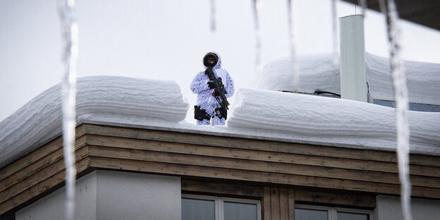 Aus einem mit Schnee bedeckten Dach steht ein Mann in weißer Jacke mit Maschinengewehr Aus einem mit Schnee bedeckten Dach steht ein Mann in weißer Jacke mit Maschinengewehr