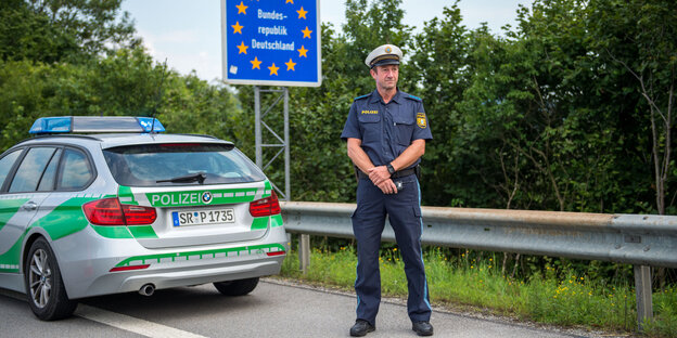 Ein Polizist steht auf der Straße vor seinem Polizeiwagen Ein Polizist steht auf der Straße vor seinem Polizeiwagen