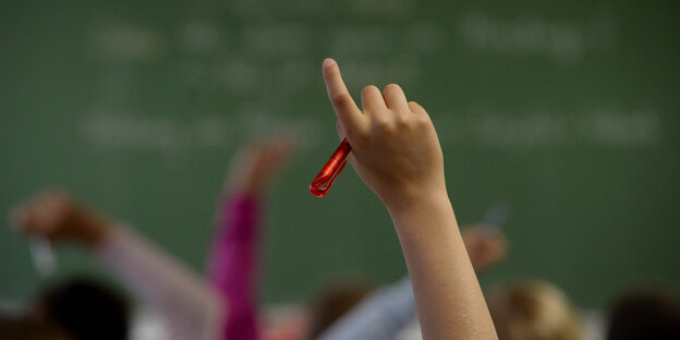 Vor einer Schultafel wird eine Hand gehoben Vor einer Schultafel wird eine Hand gehoben