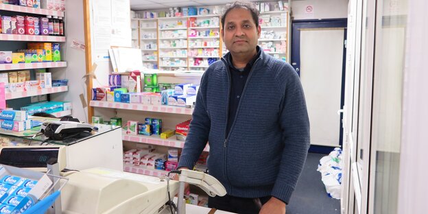 Mann steht in Apotheke hinter einer Kasse Mann steht in Apotheke hinter einer Kasse