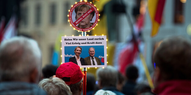 Demonstranten haben an einem Stock ein "Merkel-muss-weg"-Schild sowie ein Foto von Alice Weidel und Alexander Gauland befestigt