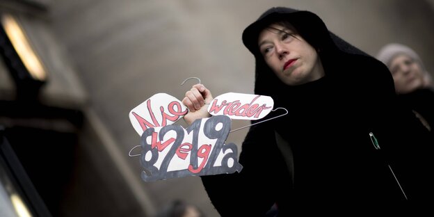 Eine Demonstrantin hält einen Drahtbügel in der Hand mit der Forderung: Nie wieder – weg mit 219a Eine Demonstrantin hält einen Drahtbügel in der Hand mit der Forderung: Nie wieder – weg mit 219a