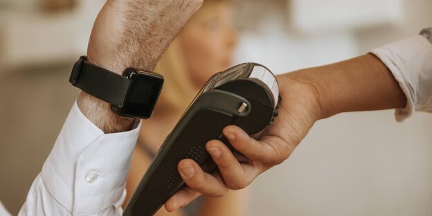 Eine Person hält ihre Smartwatch an ein Bezahlgerät Eine Person hält ihre Smartwatch an ein Bezahlgerät