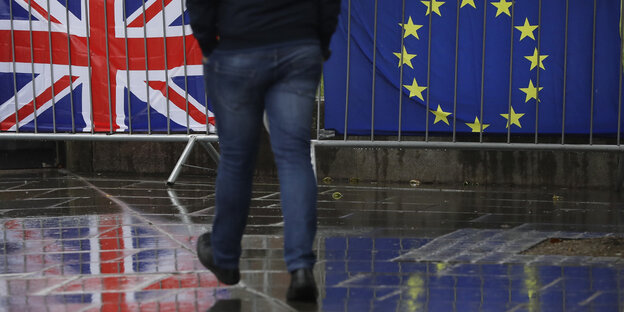 Die britische und die EU-Fahne hängen an einem Geländer, ein Passant spaziert daraufzu Die britische und die EU-Fahne hängen an einem Geländer, ein Passant spaziert daraufzu
