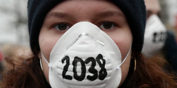 Demonstrantin mit Atemmaske, auf der 2038 steht Demonstrantin mit Atemmaske, auf der 2038 steht